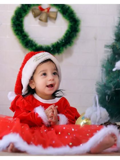 A happy baby girl in her Santa dress, surrounded by festive decorations during our special Christmas mini-sessions.