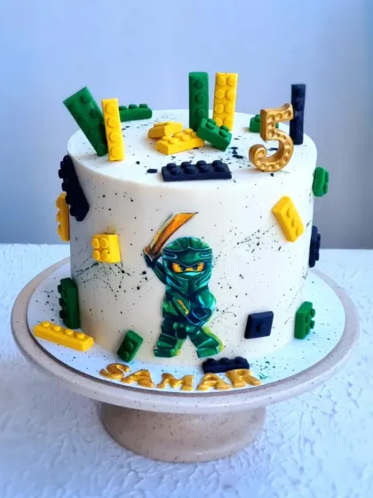 A Ninjago-themed cake with a paint splatter effect on the buttercream. The design is completed with fondant Lego bricks and a printed edible image of a ninja.