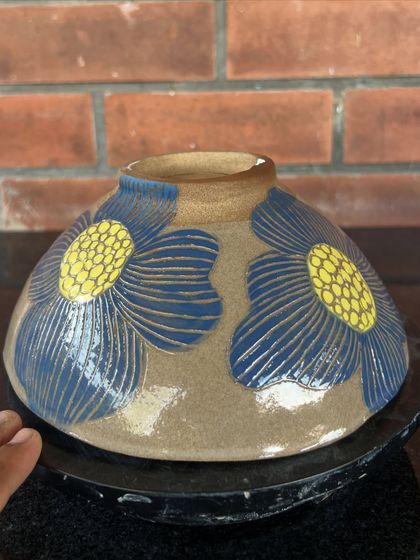 A student's hand-built bowl or planter, decorated with bold, sgraffito-carved blue and yellow flowers. The design is so cheerful and vibrant.