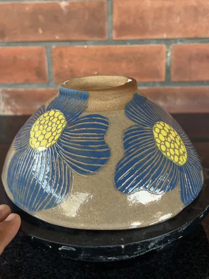 A wheel-thrown bowl decorated with large, stylized blue and yellow flowers using the sgraffito technique.