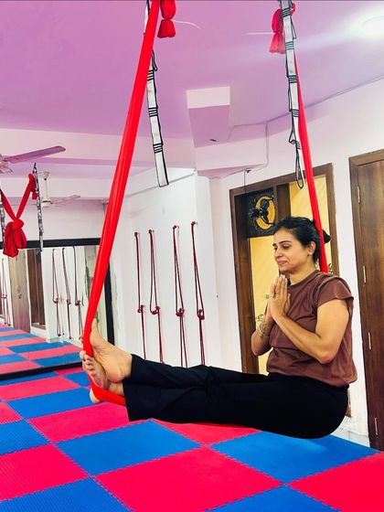 The aerial hammock provides a perfect seat for finding your center. Here, a student holds a seated prayer pose, demonstrating the calm and focus that can be achieved mid-air.