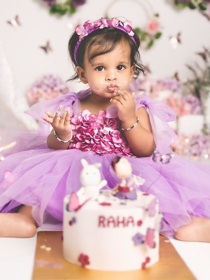 A close-up of a one-year-old girl enjoying her birthday cake during a purple butterfly-themed smash.