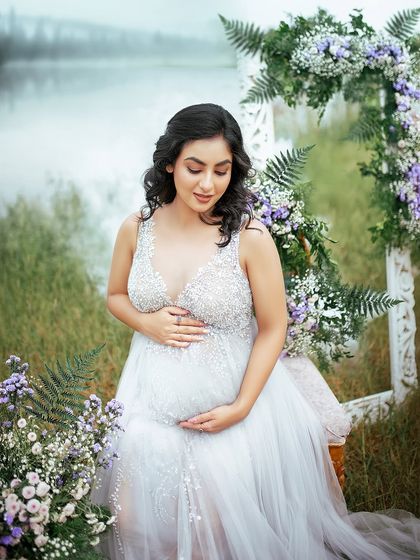 A tender moment as the mom to be cradles her belly. The soft, misty background and delicate flowers create a serene and loving atmosphere for this maternity photo.