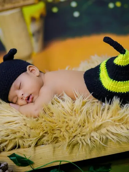 A sleepy newborn in a bee costume, nestled on a fur blanket in a wooden crate. The background hints at a Winnie the Pooh theme with "Hunny" pots.