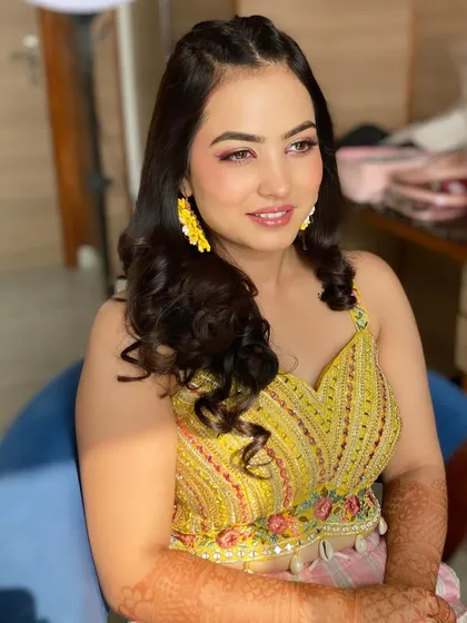 A stunning Haldi look with a pop of color on the eyes. The pink eyeshadow and fresh, dewy skin perfectly complement the yellow outfit and floral earrings.