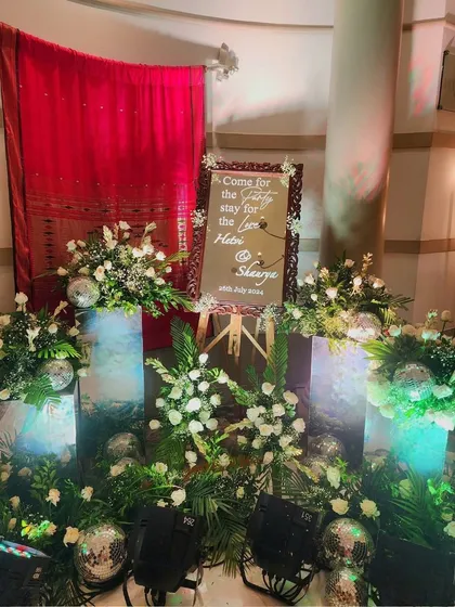 A creative welcome sign for a reception, surrounded by floral arrangements on illuminated pedestals and sparkling disco balls.