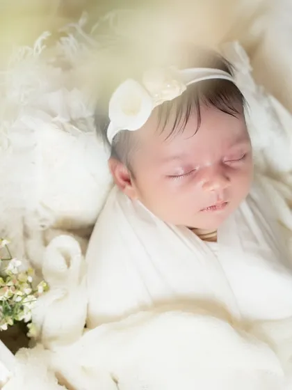 A close-up shot, with a soft focus on the foreground flowers, drawing the eye to the baby's perfectly peaceful face.