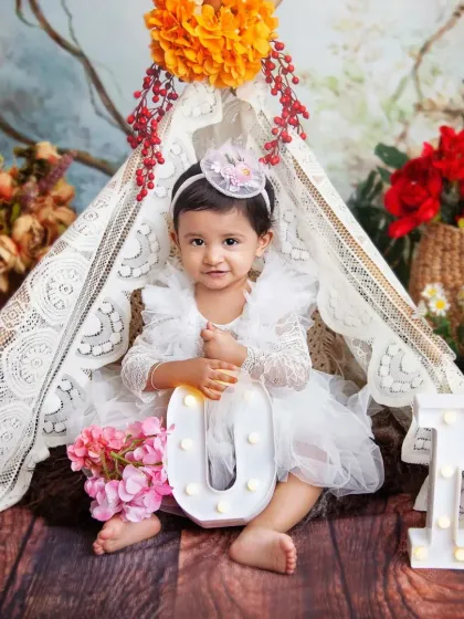 So much sweetness in one photo. This boho-chic teepee setup, surrounded by flowers, is perfect for a 'Wild One' or fairy garden theme. I love capturing these calm, classic portraits before the cake smash begins.