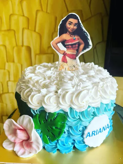 A Moana-themed cake featuring a doll-style design where the cake itself becomes her dress. The blue and white ombre rosettes create a beautiful ocean wave effect, perfect for a tropical princess party.
