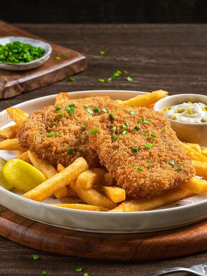 A plate of crispy fish and chips, a classic comfort meal, served with a side of tartar sauce.