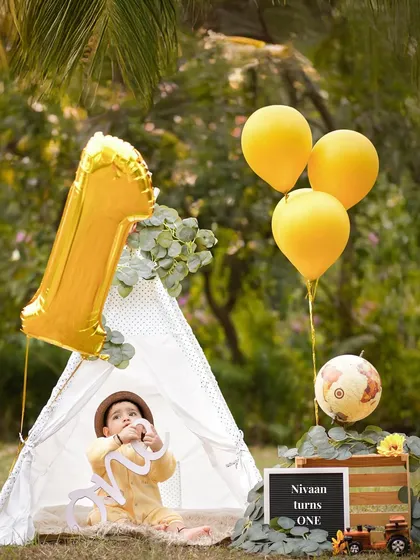Capturing a quiet moment during his outdoor first birthday session. The "Nivaan turns ONE" sign adds a personal touch to this travel and adventure-themed setup.