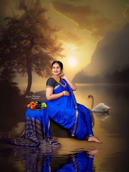 A fine art portrait that evokes a sense of peace and abundance. The mother-to-be, dressed in a beautiful blue saree, sits by a tranquil lake at sunset with a bowl of fruit.