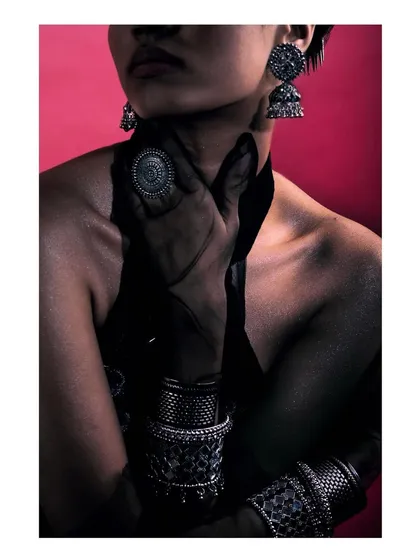 A dramatic shot for a silver jewelry campaign, inspired by Mumbai's fashion scene. The close-up focuses on the intricate details of the stacked bracelets, ring, and earrings against a bold pink background.