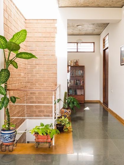 A hallway in the Samvrruddhi home, lined with plants and looking down into the central courtyard. The polished concrete floor reflects the natural light, making the passage feel bright and welcoming.