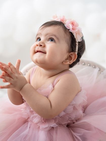 A close-up of a beautiful baby girl in her pink party dress, looking up with a sweet expression.