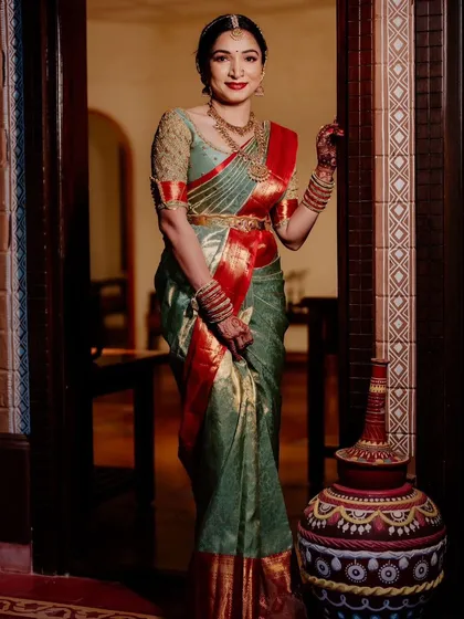 A client in a sage green and red Kanchipuram saree. Her custom blouse features delicate embroidery on sheer sleeves, adding a modern touch to her traditional look.