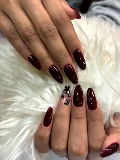 A sophisticated design featuring long, deep red almond nails with a single accent nail showcasing delicate black floral art.