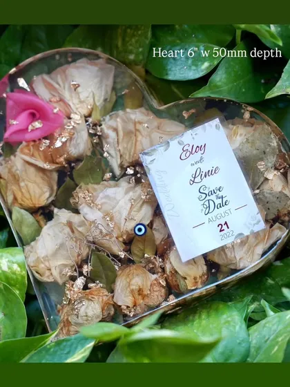 A heart-shaped resin block holding white wedding flowers and a 'Save the Date' card. It’s a perfect way to remember the very beginning of your journey together.