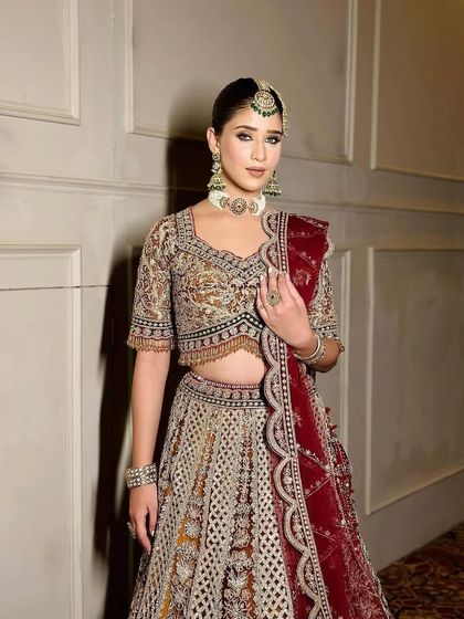 A front-facing portrait of the bride, her hands gently holding her dupatta.