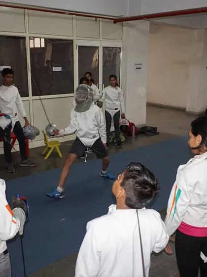 A coach demonstrates a technique to a group of young fencers during a training session. Observational learning is key before students practice the moves themselves.