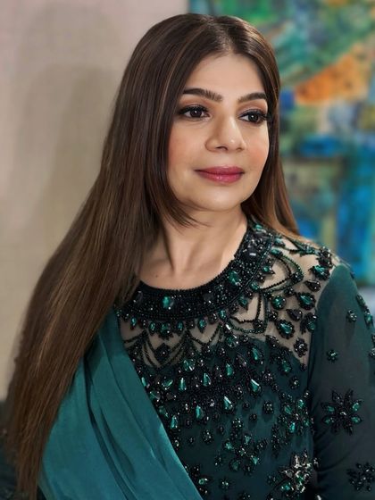 A client styled for an evening event in an elegant green dress. Her hair is styled straight with light layers and highlights, paired with a sophisticated makeup look.