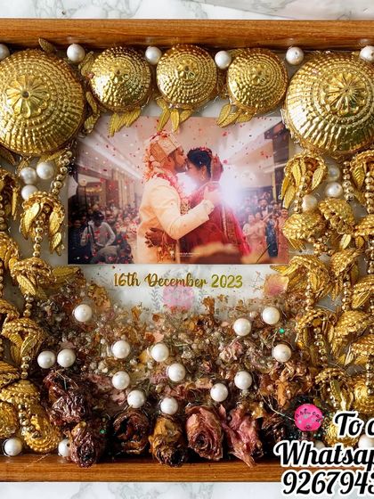 This square frame is a celebration of a bride's accessories. Her golden kaleera and varmala flowers are artfully arranged around a cherished wedding photo, dotted with pearls for an elegant finish.