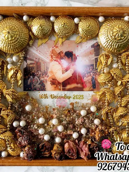 This square frame is a celebration of a bride's accessories. Her golden kaleera and varmala flowers are artfully arranged around a cherished wedding photo, dotted with pearls for an elegant finish.