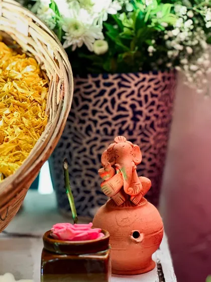 A close-up of the small details that make an event special. This shot shows a small terracotta Ganesha idol, a basket of flower petals, and fresh flowers in a vase.