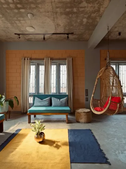 The interplay of light and shadow reveals the raw honesty of the materials. This living space in a vernacular home features exposed brick, a raw concrete ceiling, and simple wooden furniture, creating an atmosphere of warmth and authentic minimalism.