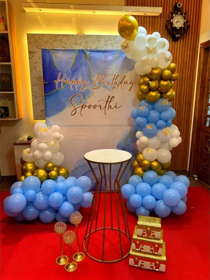 A beautiful blue, white, and gold balloon arrangement against a marbled blue backdrop for Spoorthi's birthday. This setup creates a dreamy, cloud-like effect.
