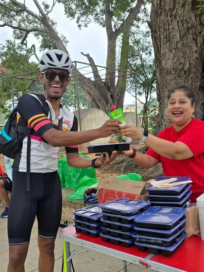 The spirit of community in action. A rider receives a packed meal and a drink from one of our smiling volunteers during the Rajyotsava 200k ride. Support is everything.