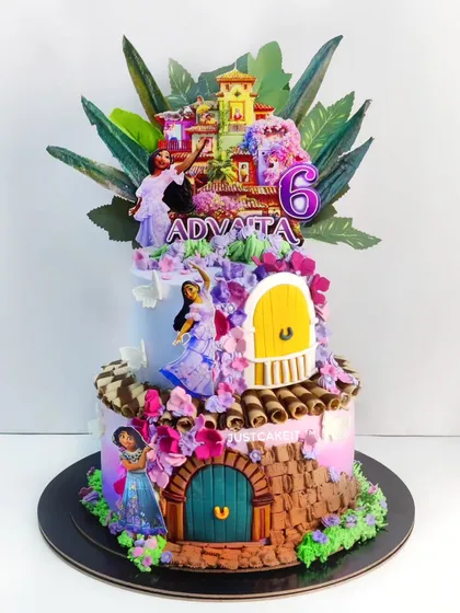 An intricate Encanto theme cake inspired by the character Isabella. This whipped cream cake is decorated with a cascade of edible flowers, wafer paper leaves, and detailed fondant doors.
