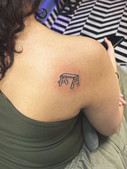 A quirky and minimalist tattoo of a small stool on the shoulder blade. Tattoos can be fun and don't always have to be serious.