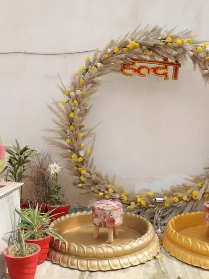 The complete Haldi setup for a silver jubilee celebration, featuring a large circular pampas grass frame and traditional brass urlis.