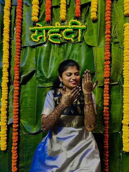 A happy bride posing against a beautiful backdrop of banana leaves and marigolds, a classic mehendi ceremony decor.