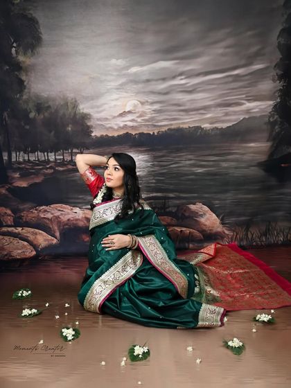 A painterly and artistic portrait. The mom-to-be, dressed in a traditional green saree, is posed against a scenic, moonlit backdrop, creating a timeless and poetic image.