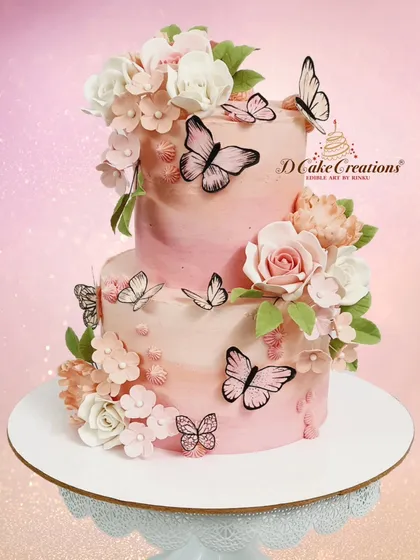 This two-tier buttercream cake is a piece of art, featuring a soft pink ombre effect adorned with delicate, hand-piped sugar flowers and whimsical wafer-paper butterflies. It’s a perfect example of how I blend classic techniques with modern elegance.