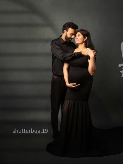 A romantic couple's portrait using creative lighting to cast a window-like shadow. The intimate embrace and the elegant black attire make this a modern and artistic maternity photo.