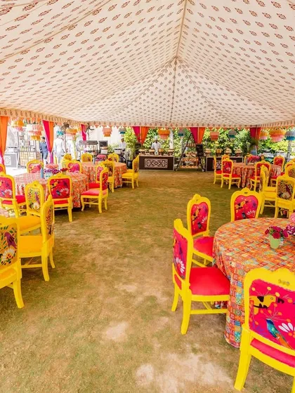 A vibrant dining area with colorful printed tablecloths and chairs, creating a cheerful and festive atmosphere for the Haldi lunch.