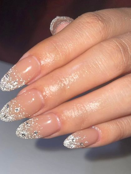 A close-up of a full-coverage silver glitter nail with rhinestone accents. This is the ultimate glamorous look for a special event.
