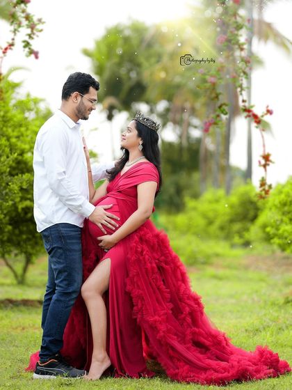 A romantic couple's portrait in a garden, with the mother-to-be in a red ruffled gown and crown.