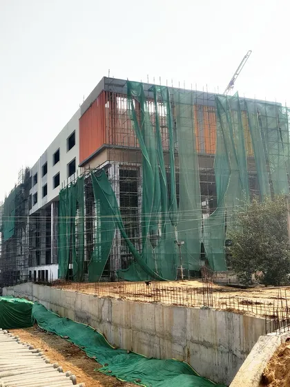 Construction in progress at an upcoming school in Gurugram. The building's structure is visible, wrapped in green safety netting, as the facade begins to take shape.