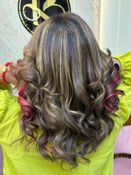 A fun and vibrant look combining blonde highlights with pops of pink. The hair is styled in curls to show off the different tones.
