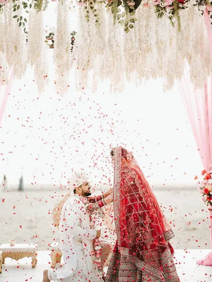 A beautiful ritual during the wedding ceremony. The bride's makeup remains impeccable, with her red veil adding a touch of traditional romance.
