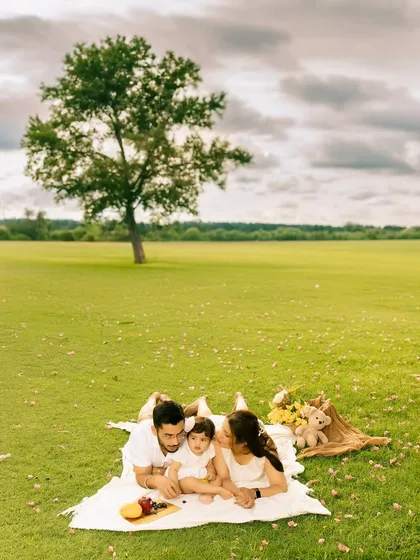 A family lies together on a picnic blanket in a vast green field under a dramatic sky. This wide-angle shot captures a sense of peace and connection, emphasizing the family in a beautiful landscape.