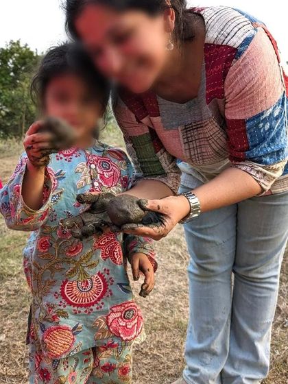 A parent and child share a moment of discovery, their hands full of clay. The fascination with mud and clay is universal and timeless.