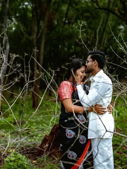 An intimate pre-wedding moment in a rustic, natural setting. The branches create a beautiful, organic frame around the couple.