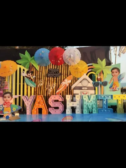 A fun and sunny beach or Hawaiian themed birthday party, with large marquee letters spelling the name "YASHVIT" and surfboard props.