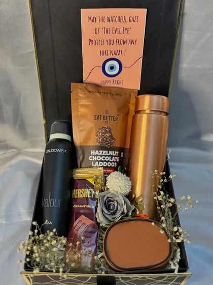 This Rakhi hamper for a brother is designed to protect and pamper. It includes an evil-eye themed card, a copper bottle, a deodorant, and healthy snacks.