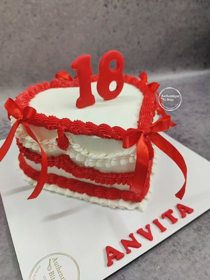 A red and white heart-shaped cake for an 18th birthday. The design features red ribbons and a layered, frilly border.